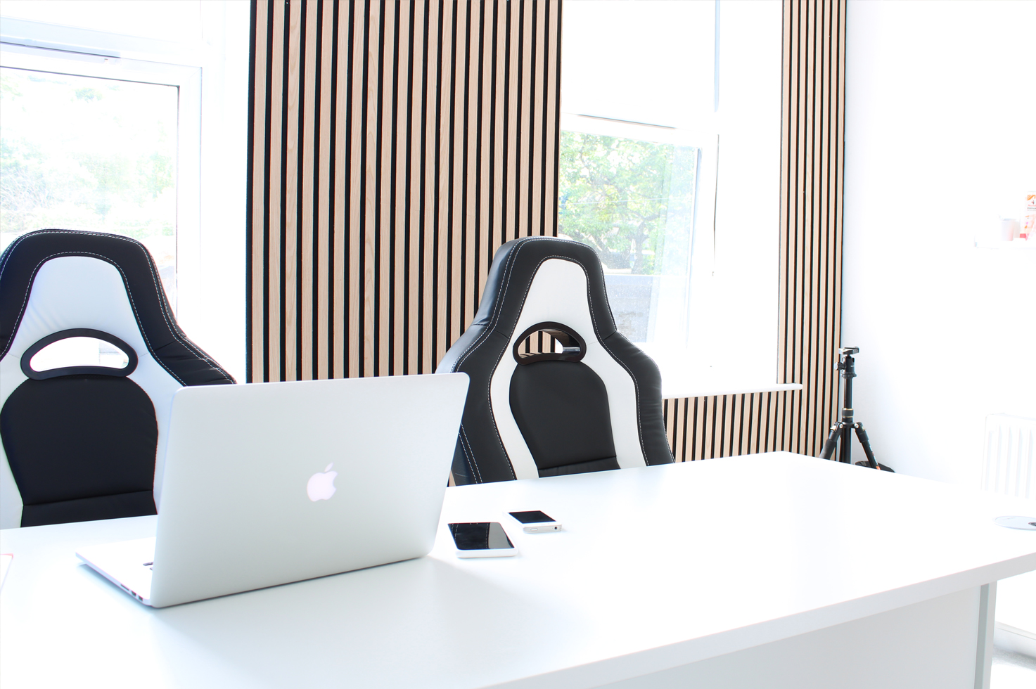 Our laptop placed on our white office desk with white accented chairs, whilst also demonstrating our wooden-slatted walls in the background.