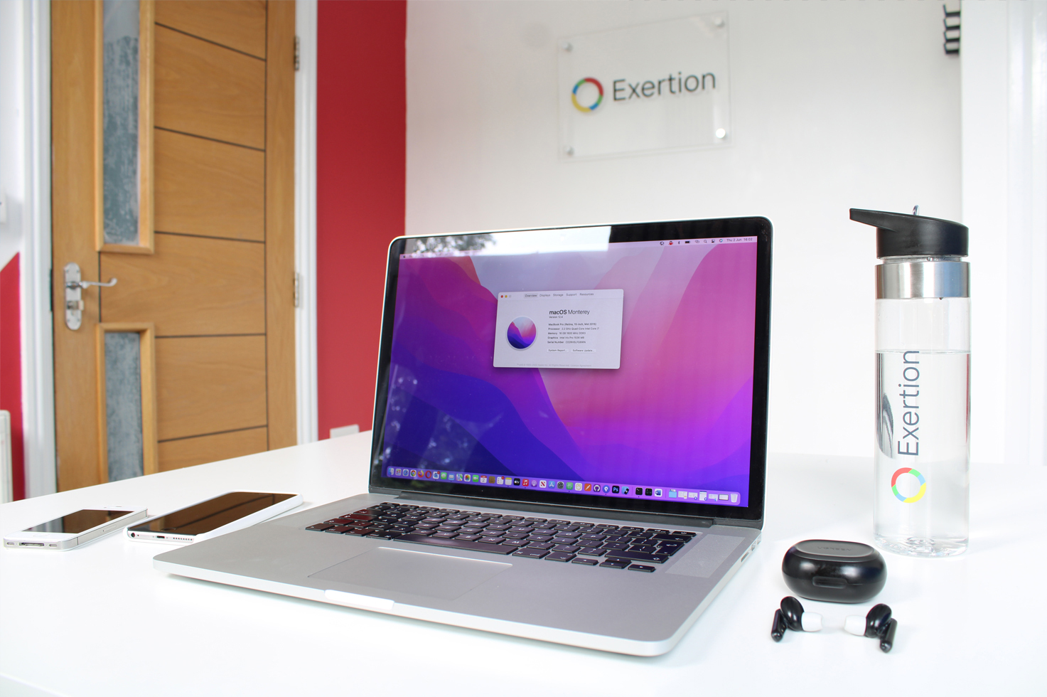 Our upgraded MacBook Pro setup in our new office, alongside a pair of wireless earphones, smartphones and our branded water bottle.