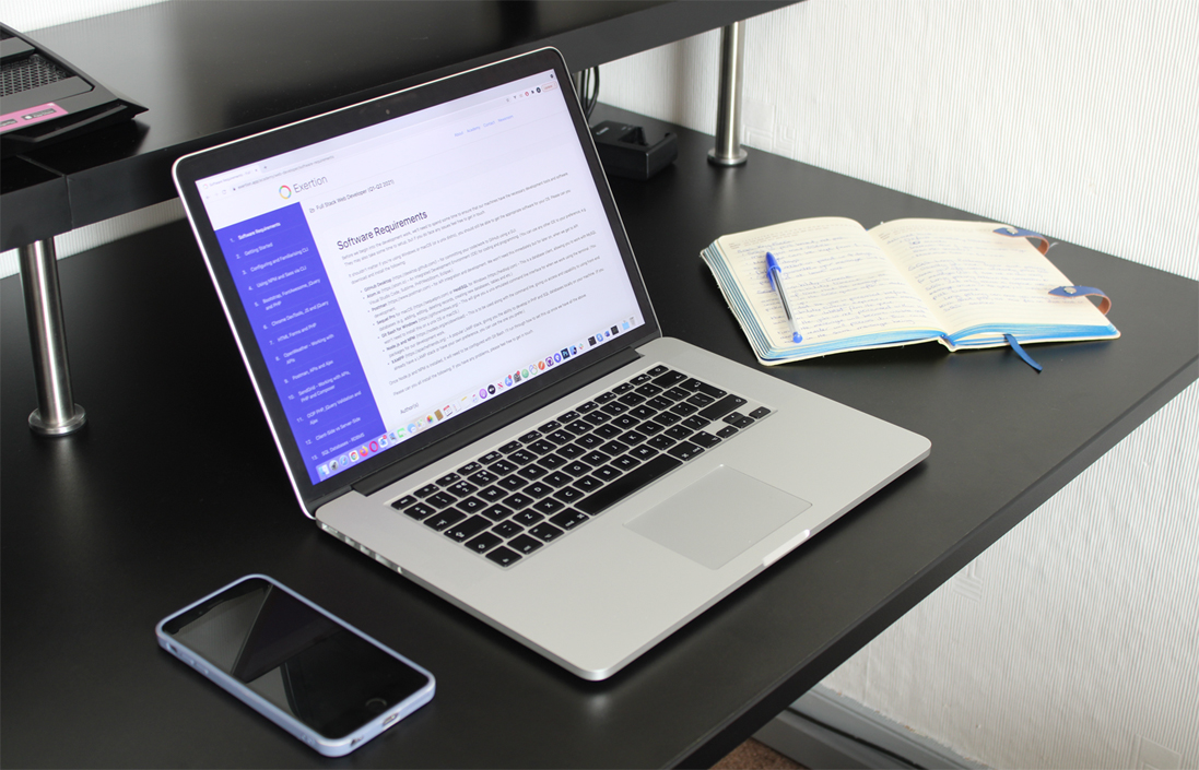 Open laptop on desk besides a smartphone and notebook with handwriting on, illustrating a studying environment.